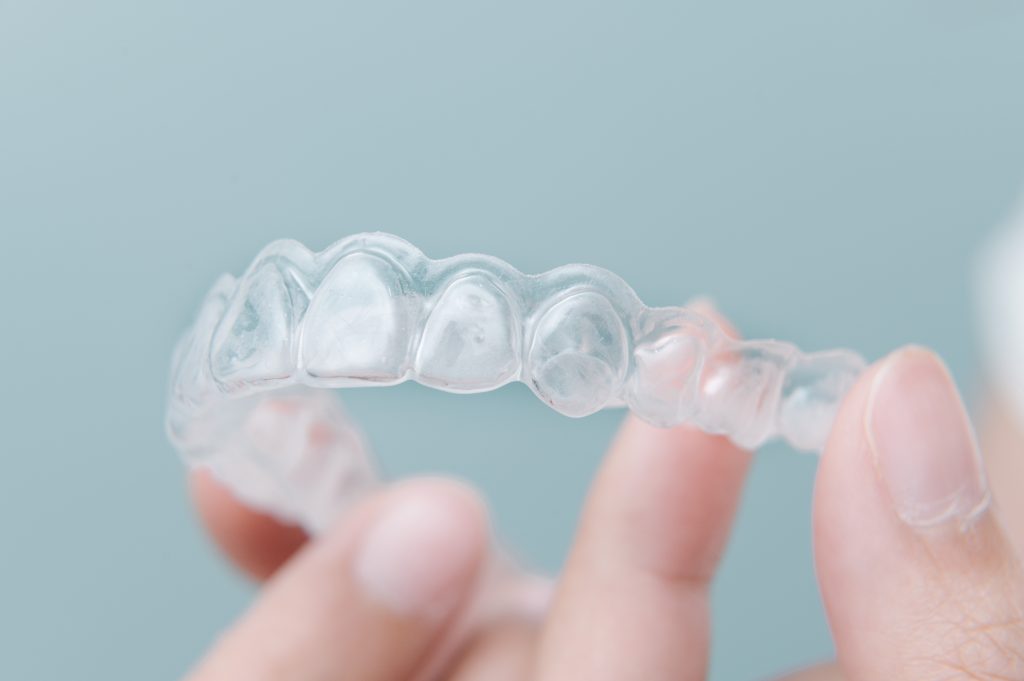 Close-up of a hand holding an Invisalign to show whether this glassy Invisalign works effectively compared to ceramic braces.